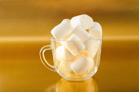 Marshmallows in a mug on a yellow background close-up and copy space. Marshmallow in a transparent mug on a gold background.の写真素材