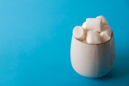 Marshmallows in a mug on a blue background close-up and copy space. Marshmallow in a cup pattern top view on a blue background.の写真素材