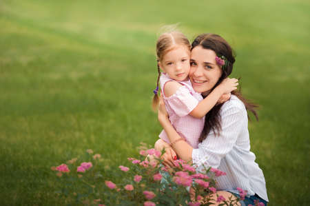 Mom and daughter with flowers close-up and copy space. Sisters near blooming flower beds in nature.