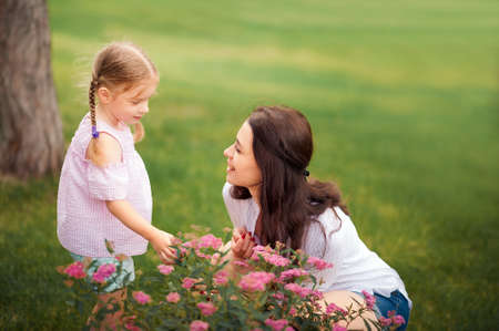 Mom and daughter with flowers close-up and copy space. Sisters near blooming flower beds in nature.の写真素材