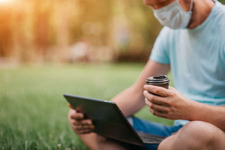 A quarantined man works remotely on a laptop. Remote work of a freelancer in a park in a mask....