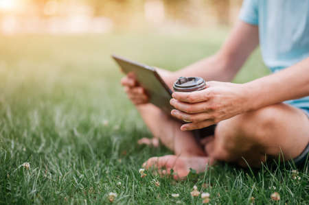 A man's hand holds a cardboard glass made from recycled material. Man with laptop in the park...