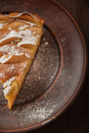 A piece of homemade pie on a plate of powdered sugar in a rustic style. Sliced apple pie with icing...