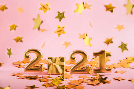 Happy New Year 2021. Numbers 2021 in gold and a gift on a pink background. Blurred focus falling stars confetti. Christmas gift in a yellow box on a pink background.の写真素材