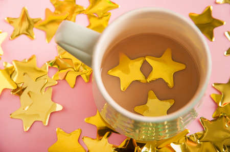 Cup with cocoa and confetti on a pink background. Confetti stars in a cup after the holiday. Holiday concept, food, drinks and copy space.の写真素材