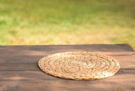Round wicker napkin for cutlery on a wooden table against the background of autumn nature. Texture table Water Hyacinth Placemat close-up and copy space.の写真素材