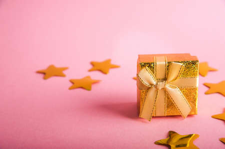 Gold box with a gift on a pink background. Gold stars confetti on a pink background. Golden gift and...