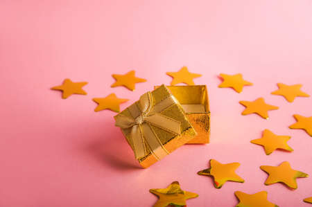 Gold box with a gift on a pink background. Gold stars confetti on a pink background. Golden gift and confetti close-up and copy space.の写真素材