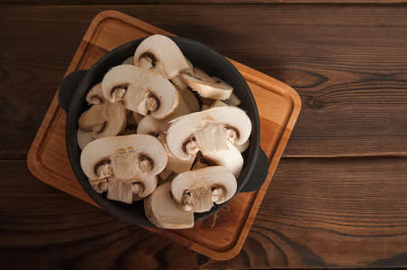 Mushrooms in a black plate on a wooden board. Chopped champignons in a cast iron skillet close-up and copy space.の写真素材