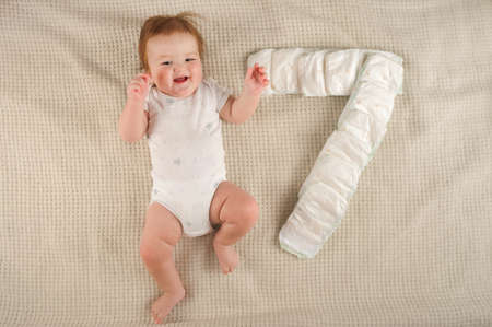 Beautiful little redhead baby in a white bodysuit on the bed close-up and copy space. Newborn by...