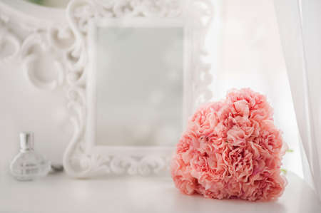 Pink flowers on the dressing table in the white bedroom. Flowers and perfumes in a bright interior. White boudoir table close up and copy space.の写真素材
