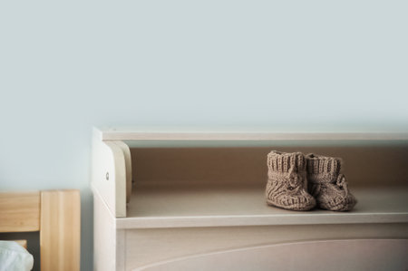 Baby booties on the shelf and copy space. Knitted boots for a newborn on a chest of drawers...