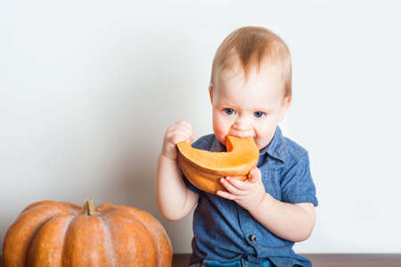 Baby in denim overalls and pumpkin. Toddler and concept of pumpkin puree, harvest, food allergies, healthy eating and first feeding .の写真素材