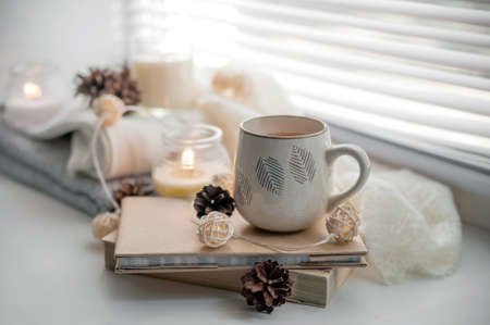 ? ug of tea, white sweater and books with candles on windowsill. Cozy autumn concept.