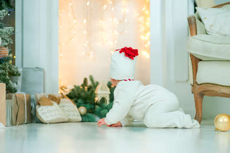 Baby crawls against background of Christmas tree and fireplace in garland. Infancy, babyhood at home at Christmas. Baby's first christmasの写真素材