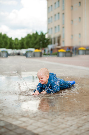 Happy toddler walks through the puddles in blue jumpsuit with splashes close-up and copy space.の写真素材