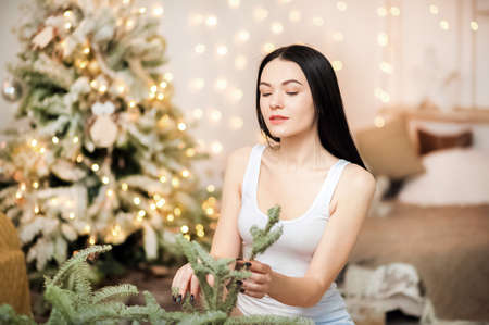 Beautiful young girl in bedroom for New Year on background of Christmas tree. Christmas Eve, decoration, holiday at home.の写真素材