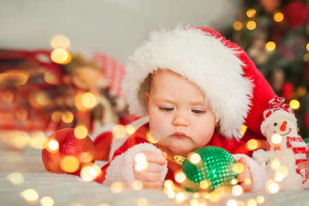 Baby boy dressed as Santa Claus for Christmas plays with wooden train and Christmas decorations in living room.の写真素材