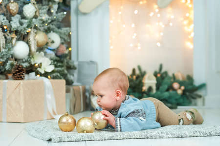Baby boy in blue sweater crawls background of Christmas tree and fireplace in garland. Infancy, babyhood at home at Christmas. Baby's first christmasの写真素材