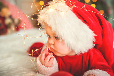 Baby boy dressed as Santa Claus for Christmas plays with wooden train and Christmas decorations in living room.の写真素材