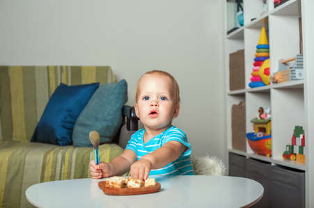 Toddler boy at table eating pie slices close-up and copy space. Baby with spoon and first lure.
