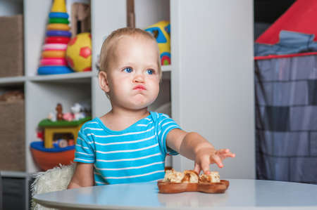 Toddler boy at table eating pie slices close-up and copy space. Baby with spoon and first lure.の写真素材