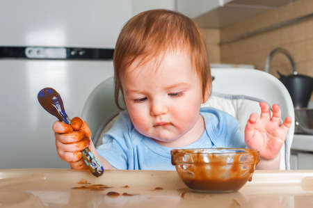 Handsome red-haired baby eating in children's chair. First feeding children with porridge, vegetables, fruits, meatの写真素材
