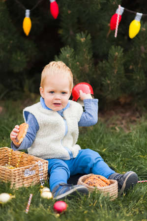 Cute toddler eating Christmas cookies with milk in decorated backyard close-up and copy space.