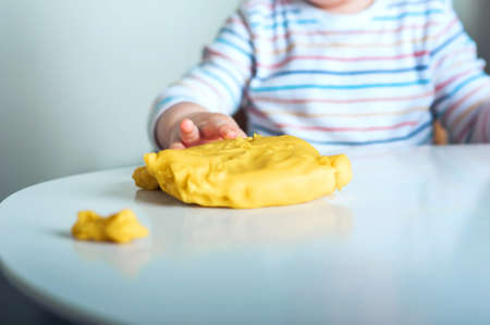 Toddler boy playing yellow plasticine Play-Doh in playroom close-up and copy space.の写真素材
