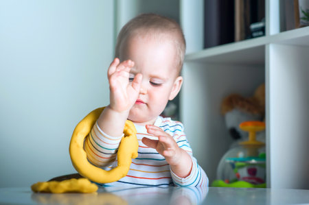 Toddler boy playing yellow plasticine Play-Doh in playroom close-up and copy space.の写真素材
