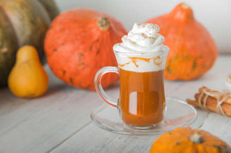 Cup with foam and cinnamon on background of pumpkins. Pumpkin autumn warming drink close-up and copy space.の写真素材