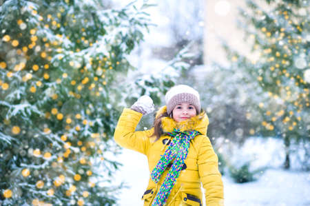 Happy girl in yellow jacket plays with snow. Children games in winter..の写真素材
