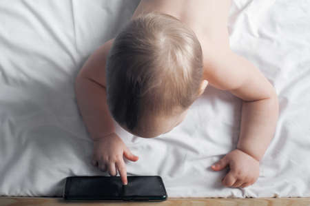 Child 1 year old on bed with mobile phone close-up.の写真素材