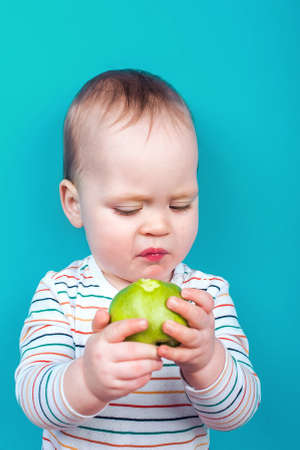Handsome baby boy with apple on blue background. Concept of healthy eating and first feeding of children, baby food additives, allergies ..の写真素材