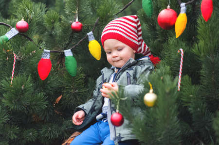 ? ute toddler decorating Christmas tree in backyard. Child in Santa Claus hat for New Year close-up. DIY felt garland.の写真素材