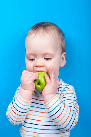 Handsome baby boy with apple on blue background. Concept of healthy eating and first feeding of children, baby food additives, allergies ..の写真素材