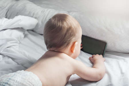 Child 1 year old on bed with mobile phone close-up.の写真素材