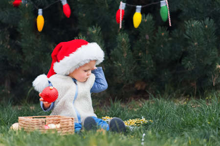 ? ute toddler decorating Christmas tree in backyard. Child in Santa Claus hat for New Year close-up....