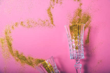 Two champagne glasses and gold glitter on pink background. Concept of holiday for couple ..の写真素材