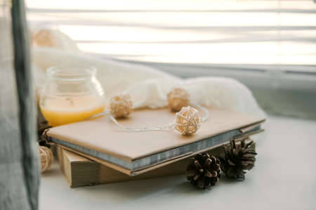 Burning candles and white sweaters on windowsill. Cozy autumn and winter concept, window with blinds.の写真素材