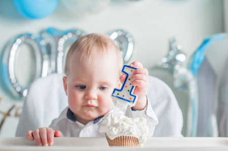 Cute toddler boy for first year of birth eating birthday cupcake with 1 candle close-up and copy space.