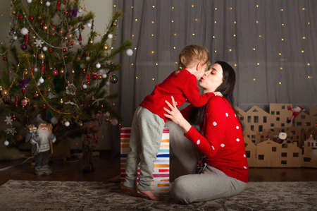 Young happy mom and daughter in red sweaters open gifts in bags at home. Christmas mood, DIY home decor from cardboard.の写真素材