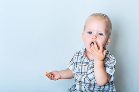 Toddler boy in blue shorts and shirt eating cookies close-up and copy space.
