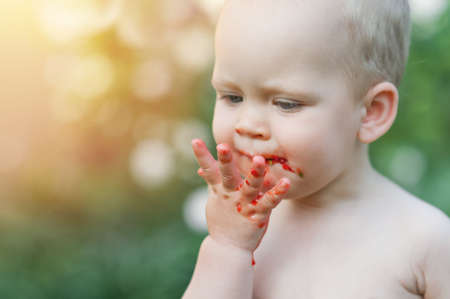 Baby eats strawberries and raspberries. Toddler face in food close-up.の写真素材