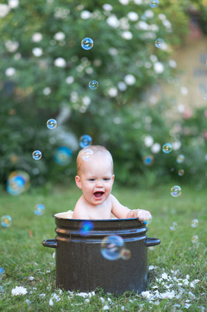 Toddler activity outside summer. Cute baby boy bathes in basin with foam and soap bubbles.の写真素材