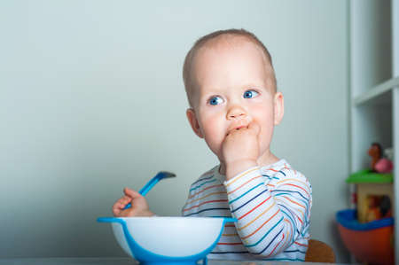 Toddler boy eats with spoon at table..の写真素材