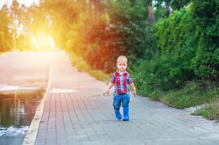 Toddler boy in rubber boots lies and runs through puddles after rain.の写真素材