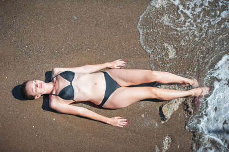 Young beautiful woman in black swimsuit on background of ocean. Summer holidays at sea.の写真素材