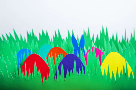 Lots of colorful paper Easter eggs in grass and bunny ears.