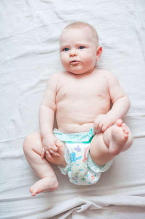 Smiling baby 7 months old in diaper on bright bed close-up.